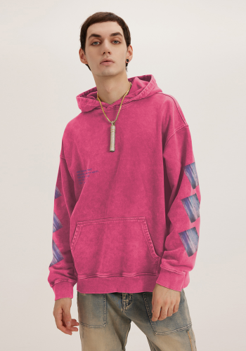 Produktfoto mit Link: Männliches Model von vorn trägt einen verwaschenen, dicken Kapuzenpullover in einem satten Pink. Aufnahme bis zu den Oberschenkeln. Der Mann steht vor neutral beigem Hintergrund. Auf den Ärmeln finden sich jeweils drei schräge Aufdrucke des Ozeans in Maui, Hawaii. Im Brustbereich ergänzt der dunkelblaue Text samt Logo die Verortung in Hawaii samt Koordinaten. Produkt namens 