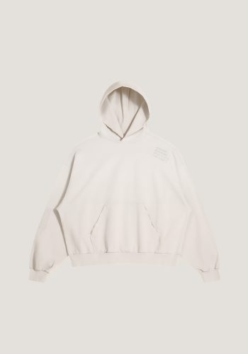 Produktfoto mit Link: Flatlay-Fotografie der Vorderseite eines ausgefransten, stylischen beigen Kapuzenpullovers vor neutralem beigen Hintergrund. Ein Text über Amsterdam ist auf der Schulter und auf dem rechten Ärmel dezent aufgedruckt. Produkt namens 