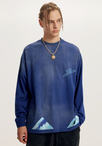 Produktfoto mit Link: Männliches blondes Model von vorn trägt einen Pullover in sattem Blau. Aufnahme bis zu den Oberschenkeln. Der Mann steht vor neutral beigem Hintergrund. Auf dem Pullover finden sich unten vor dem Saum dreieckige Aufdrucke der beeindruckenden eisigen Landschaft von Cuernos del Paine in Chile. Die Cuernos del Paine sind markante, hornförmige Granitgipfel im chilenischen Nationalpark Torres del Paine. Auf der linken Seite auf Brusthöhe ergänzt der hellblaue Text samt Logo die Verortung in Chile samt Koordinaten. Produkt namens 