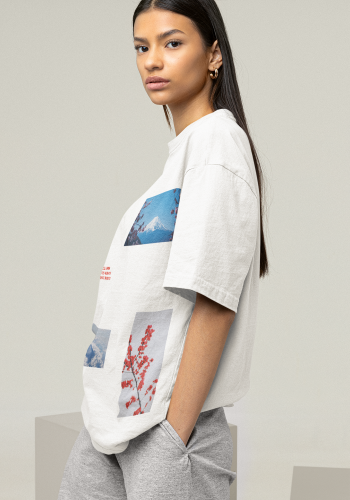 Produktfoto mit Link: Weibliches Model mit langen dunklen Haaren von seitlich-vorn steht lässig vor neutral-beigem Hintergrund. Sie trägt ein weißes Oversize-T-Shirt. Auf dem T-Shirt sind verschiedene rechteckige Fotos zu sehen, die versetzt verteilt sind. Sie zeigen japanische Motive, wie zum Beispiel einen Tden Berg Fuji in verschiedenen Perspektiven und einen roten Zweig. Auf der rechten Brustseite sind die Koordinaten des Mount Fuji aufgedruckt Produkt namens 