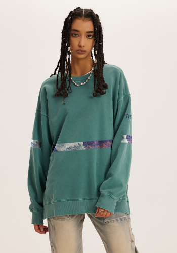 Produktfoto mit Link: Dunkelhäutiges attraktives weibliches Model von vorn mit langen Rasta-Haaren trägt einen blaugrünen Pullover mit blau-braun-weißem Querstreifen in der Mitte. Aufnahme bis zu den Oberschenkeln. Die Frau steht vor neutral beigem Hintergrund. Auf den Ärmeln setzt sich der Streifen fort. Dort ist auch das Places/Pieces-Logo in Dunkelblau aufgestickt. Die Streifen zeigen einen Ausschnitt des Wasserfalls 