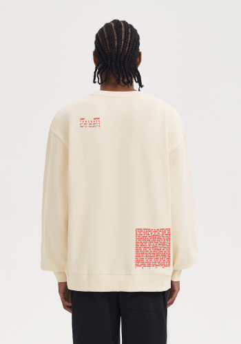 Produktfoto mit Link: Männliches dunkelhäutiges Model von hinten trägt einen beigen Pullover mit rotem Aufruck. Aufnahme bis zu den Oberschenkeln. Der Mann steht vor neutral beigem Hintergrund. Ein Text erzählt von den Flamingos, die im Natronsee in Tansania leben (rechts unten auf dem Pullover) und ein Text zeigt die Koordinaten des Ortes (links oben an der Schulter des Pullovers) Produkt namens 