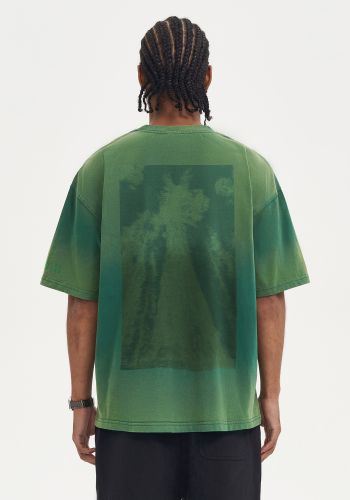 Produktfoto mit Link: Aufnahme eines dunkelhäutigen Mannes von hinten vor neutral-beigem Hintergrund, der ein übergroßes grünes Batik-T-Shirt trägt. Auf dem Rücken ist ein grün verfärbtes Foto eines Sequoia-Baumes zu sehen, das Ton-in-Ton mit dem grünen Hintergrund des T-Shirts verschwimmt. Produkt namens
