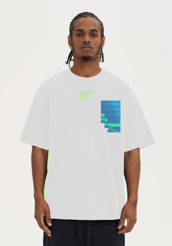 Produktfoto mit Link: Männliches dunkelhäutiges Model von vorn trägt ein weißes übergroßes T-Shirt. Aufnahme bis zu den Oberschenkeln. Der Mann steht vor neutral beigem Hintergrund. Auf dem T-Shirt ist auf der linken Seite auf Höhe der Brust der Himmel am Nordpol aufgedruckt. Das blau-grüne Foto zeigt das Nordlicht und wurde nach unten dupliziert, sodass das Motiv drei mal zu sehen ist und so eine unwirkliche Wirkung erzeugt. Mittig über der Brust finden sich die Koordinaten des Nordpols in gelber und grüner Schrift, die sich überlagern. Die Seitennaht auf der rechten Seite des T-Shirts ist in neongrün eingearbeitet. Produkt namens 