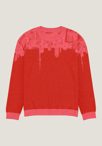 Flatlay-Aufnhame eines Strickpullovers in sattem Rot mit korallenfarbenen Ärmeln und Kragen von vorn (korallenfarben ist ein mattes, mittleres Rosarot). In den Pullover ist Motiv eingearbeitet, das oben um den ganzen Pullover geht. Der Pullover zeigt die Skyline von Toronto, aber auf den Kopf gestellt, im beschriebenen Korallen-Rosarot. Das Motiv geht von vorn über beide Ärmel bis nach hinten. Produkt namens 